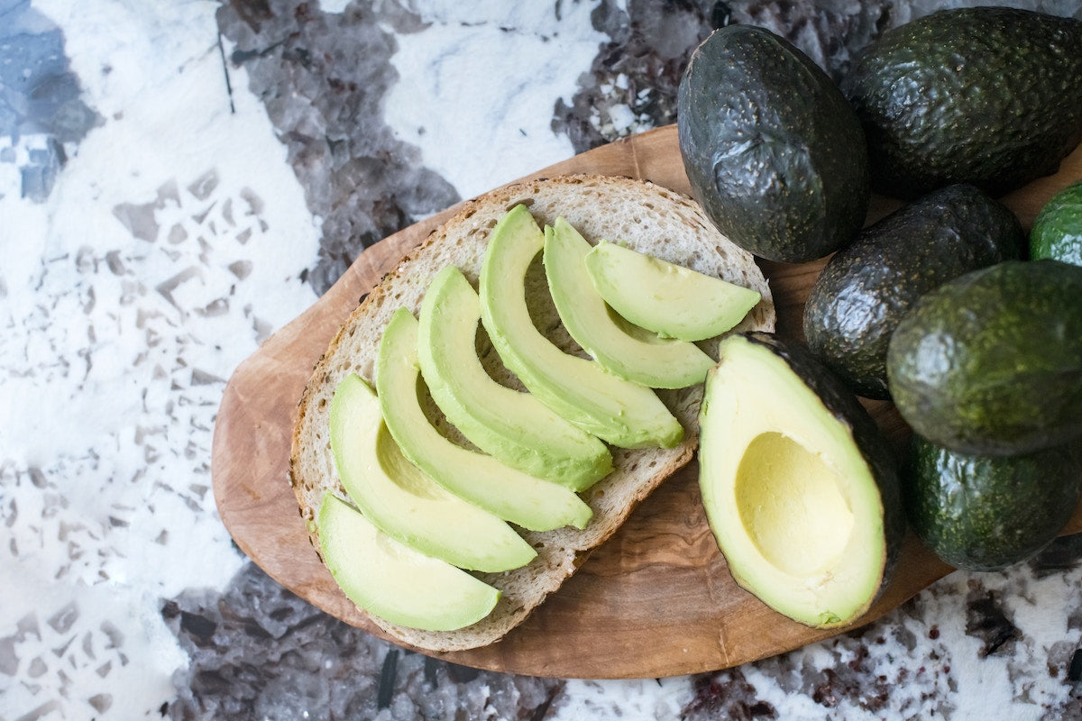 Sliced avocados on a board with whole avocados.