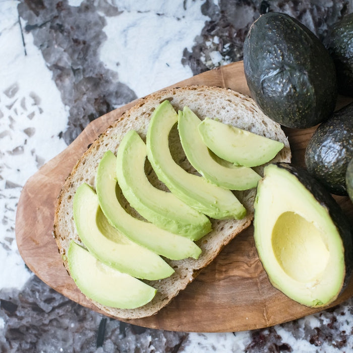 Sliced avocados on a board with whole avocados.